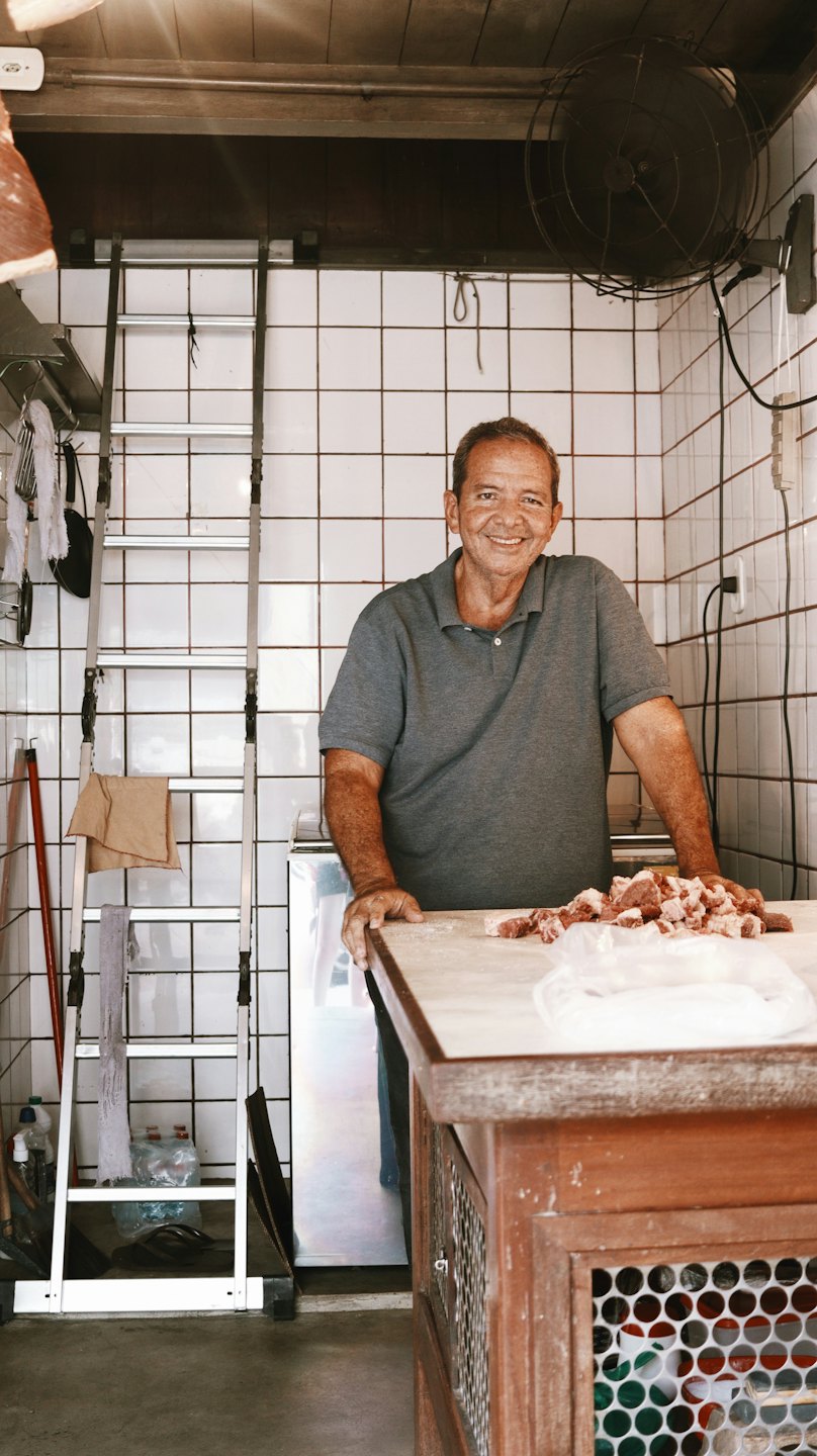 Carnicero sonriendo detrás de un mostrador con carne fresca.